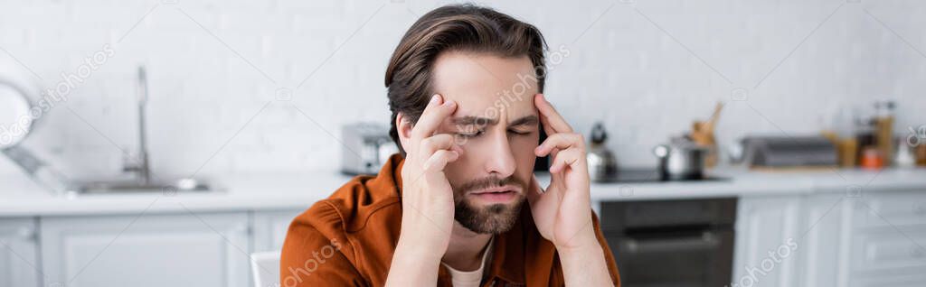 man touching head while suffering from headache with closed eyes in kitchen, banner