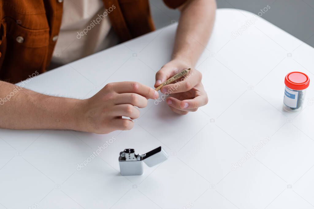 cropped view of man making joint with medical cannabis near lighter on table