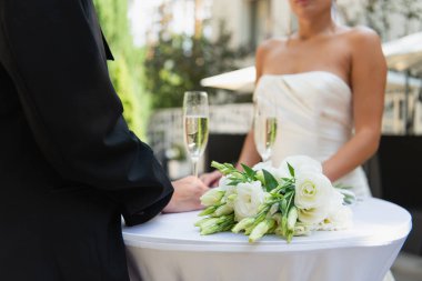 Takım elbiseli lezbiyen bir kadının düğün buketinin, şampanyanın ve kız arkadaşının yanında dikilirken çekilmiş görüntüsü. 
