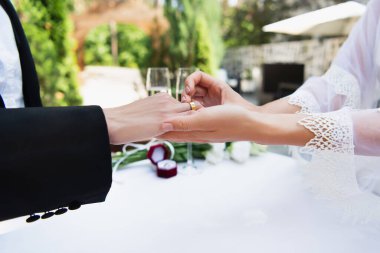 Duvak takmış lezbiyen bir kadının açık hava düğününde kız arkadaşının parmağına yüzük takması.