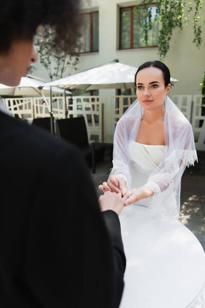 Lesbian woman in wedding dress wearing ring on finger of african american girlfriend outdoors 