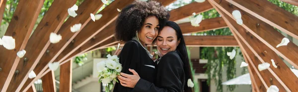 非洲裔美国女同性恋者抱着快乐的女朋友 花束飘落在公园的花瓣下 横幅上 — 图库照片