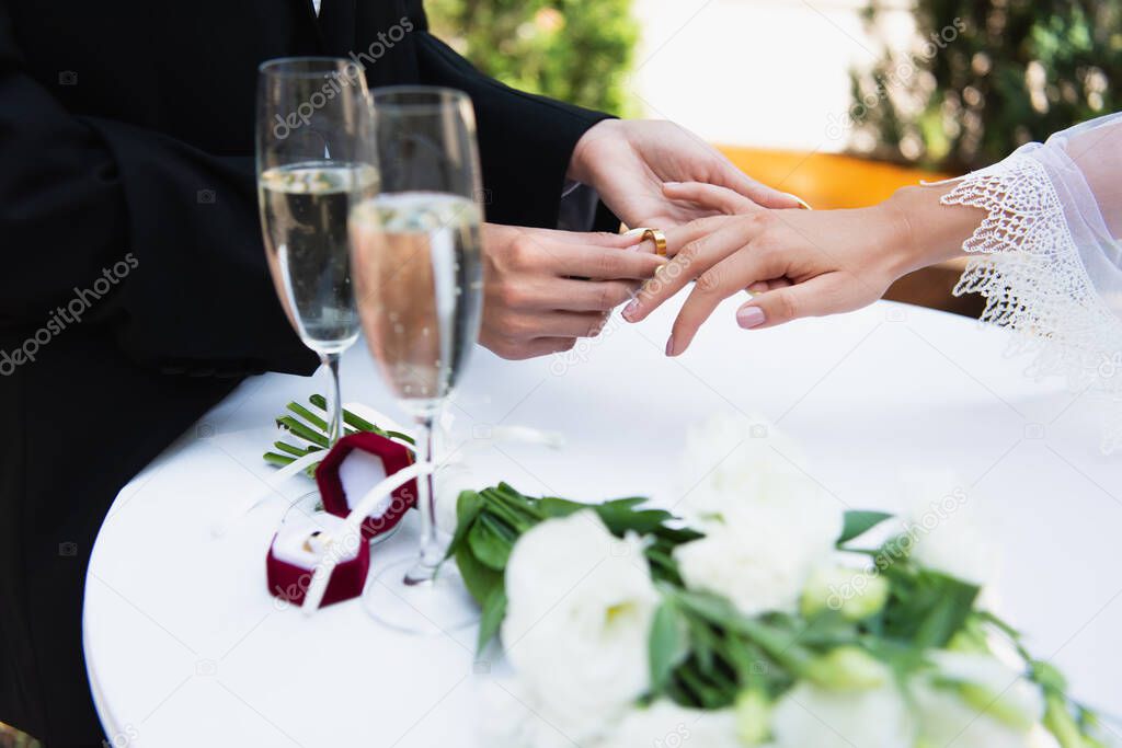 Cropped view of lesbian woman wearing wedding ring on finger of girlfriend near champagne and bouquet 