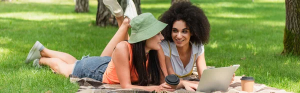 Uśmiechnięta Międzyrasowa Para Lesbijek Pomocą Urządzeń Pobliżu Papierowych Kubków Kocu — Zdjęcie stockowe