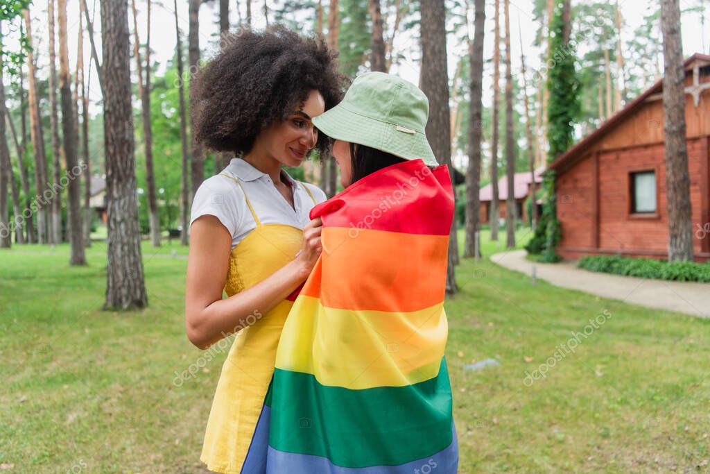 Smiling african american woman hugging girlfriend in lgbt flag outdoors
