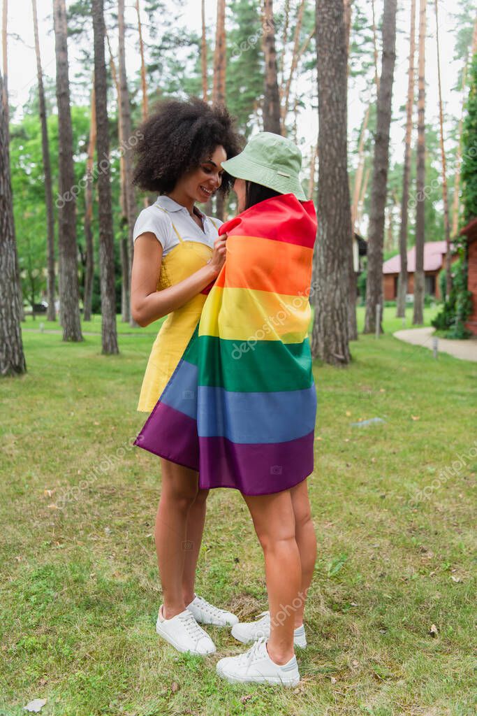 Positive african american woman hugging girlfriend in lgbt flag in park
