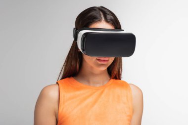 VR kulaklıklı genç esmer kadın, gri renkte izole edilmiş.