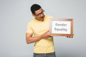 užaslý africký Američan drží plakát s písmem rovnosti pohlaví izolované na šedé