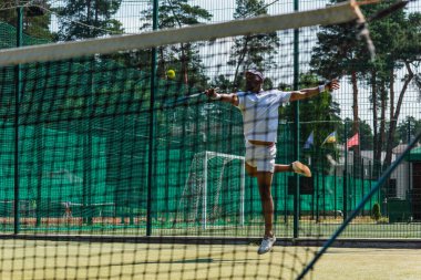 Ağ kenarında tenis oynarken atlayan Afrikalı Amerikalı sporcu 