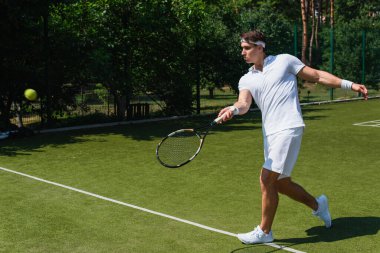 Atletik sporcunun sahada bulanık topun yanında raket tutuşu yan görünüm