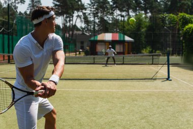 Raketli bir sporcu, dışarıda bulanık Afrikalı Amerikalı bir arkadaşla tenis oynuyor. 
