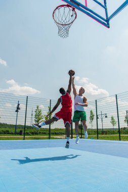 Sokak basketbolu oynarken atlayan ırklar arası adamların geniş açı görüntüsü 