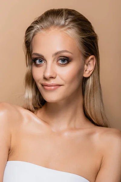 blonde woman with perfect skin and makeup smiling at camera isolated on beige