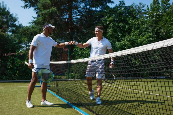Neşeli çoklu etnik tenis oyuncuları kalenin yanında yumruk tokuşturuyor. 