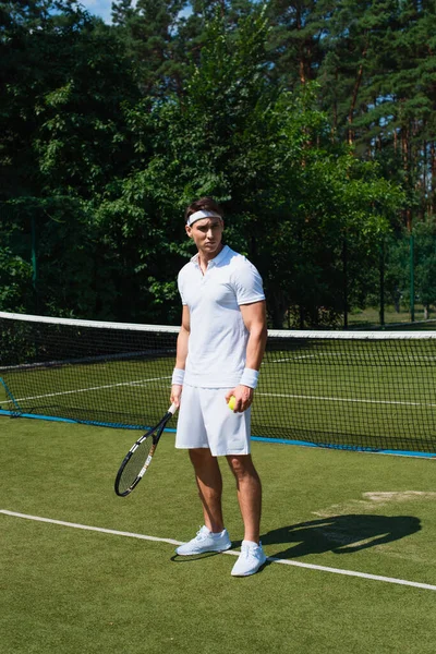 身穿白色运动服的年轻运动员拿着网球和球拍在场上 — 图库照片