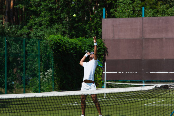 African american sportsman holding racket near ball on court 