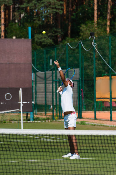 Африканский американский теннисист бросает мяч возле размытой сетки 