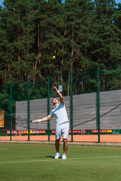 Молодой спортсмен с ракеткой бросает мяч во время игры в теннис на корте 