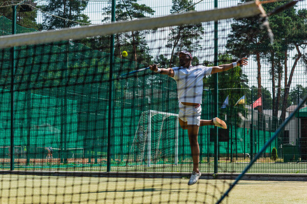 African american sportsman jumping while playing tennis near net 