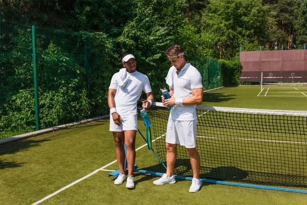 Jugadores Tenis Interracial Sosteniendo Botellas Deportivas Cancha — Foto de Stock