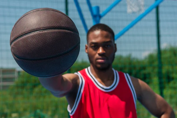 Basketball ball in hand of blurred african american sportsman outdoors
