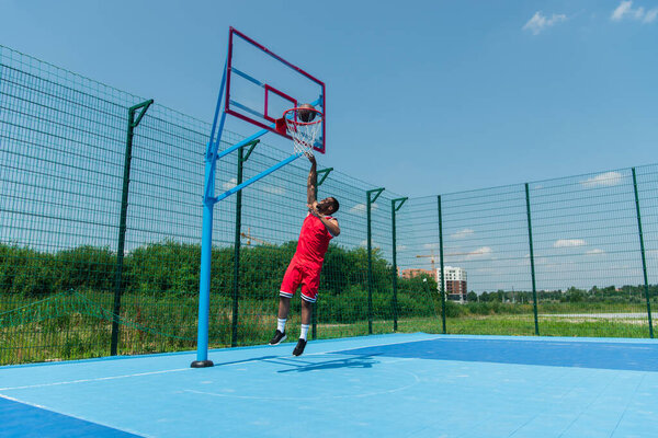 African american sportsman jumping under hoop and ball on basketball playground 