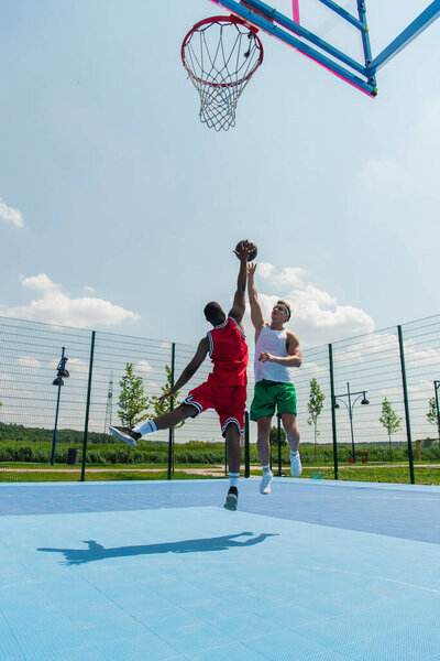 Wide angle view of interracial men jumping while playing streetball outdoors 