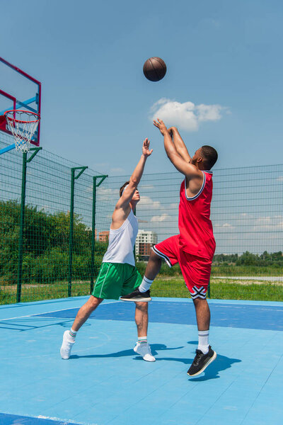 Young interracial men playing streetball on outdoor playground 