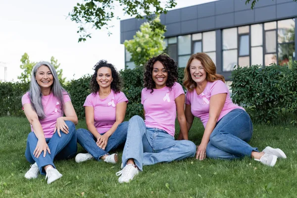 Happy Interracial Women Pink Ribbons Shirts Sitting Grass — Stock Photo, Image