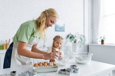 Mutfakta kızıyla yemek pişirirken yumurta kıran bir kadın.
