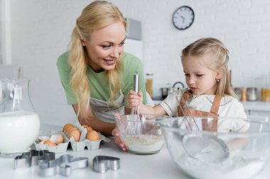 Mutfakta annenle yemek pişirirken kasede malzemeleri karıştıran bir kız.