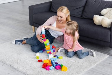 Çocuk, annesinin evinin zemininde yapı taşlarından kule yapıyor.