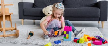 child in princess costume playing with magic wand and colorful building blocks on floor, banner clipart