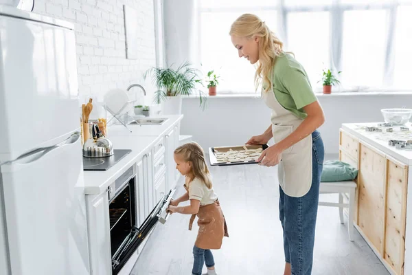 Side View Little Girl Opening Electric Oven Mom Raw Cookies — Stock Photo, Image