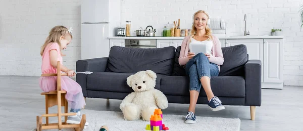 Mujer Feliz Escuchando Música Sofá Cerca Hija Montar Caballo Mecedora — Foto de Stock