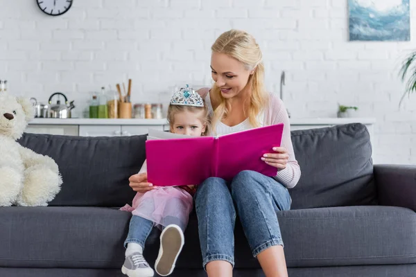 Mom Reading Book Daughter Toy Crown While Sitting Sofa Home — Stock Photo, Image