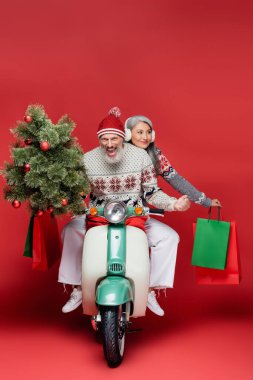 Mutlu orta yaşlı bir adam Asyalı karısının yanında Noel ağacı tutarken kırmızı motosiklete biniyor. 