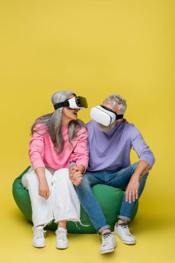 Irklar arası ve neşeli orta yaşlı çift, vr kulaklıklı, sarı koltukta oturuyorlar. 