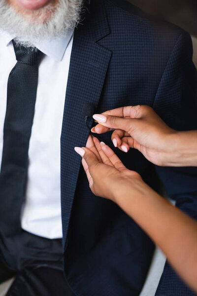 cropped view of african american assistant adjusting microphone on suit of bearded businessman