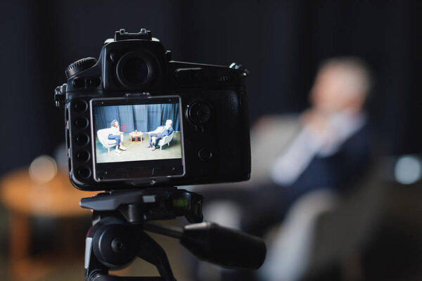 digital camera with african american journalist talking with businessman in suit during talk show on screen 