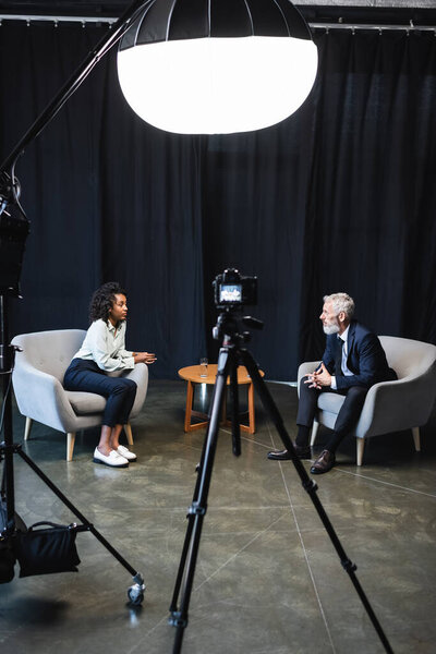 брюнетка африканская американская журналистка сидит в кресле и разговаривает с гостем в студии 