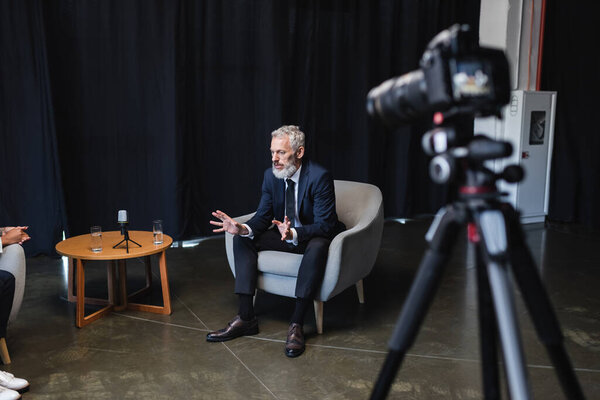 businessman gesturing while talking near african american journalist in studio 