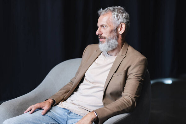бородатый бизнесмен сидит в сером кресле во время интервью