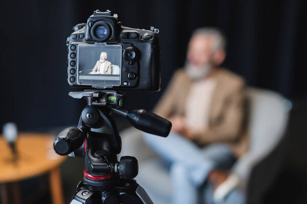 modern digital camera on tripod with businessman sitting in armchair on screen 