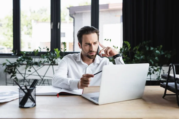 Seriöser Geschäftsmann Zeigt Auf Laptop Während Büro Mit Dem Handy — Stockfoto