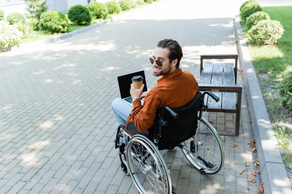 Mozgássérült Férfi Mosolyog Kamera Miközben Tolószékben Papír Pohár Laptop — Stock Fotó