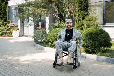 Dışarıda kameraya gülümseyen tekerlekli sandalyedeki pozitif engelli asker