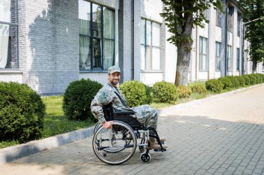 young handicapped veteran in wheelchair smiling on city street clipart