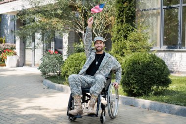 Genç ve mutlu engelli bir gazi tekerlekli sandalyede oturuyor. Elinde küçük bir Amerikan bayrağı var.