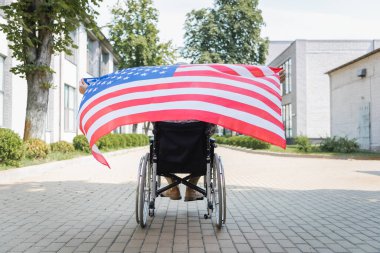 back view of handicapped soldier in wheelchair holding usa flag on city alley clipart
